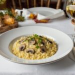 Wine with food Mushroom risotto Porcini mushrooms, creamy risotto, Sauvignon Blanc, wooden table, Mediterranean autumn light