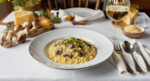Wine with food Mushroom risotto Porcini mushrooms, creamy risotto, Sauvignon Blanc, wooden table, Mediterranean autumn light