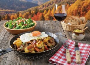 Wine served with a meal of South Tyrolean farmer's beef and potatoes in a pan, accompanied by a glass of Vernatsch on a rustic wooden table with mountain views