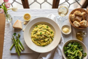 Asparagus risotto with green asparagus and lemon gremolata in a cream-colored plate, Soave Classico white wine glass, northern Italian marble setting