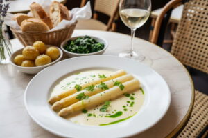 White asparagus sous-vide with beurre blanc and herb oil, close-up on a cream-colored plate, Parisian bistro setting
