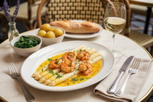 White asparagus with prawns and saffron butter sauce on a white bistro plate, with Albariño white wine glass, Parisian bistro setting
