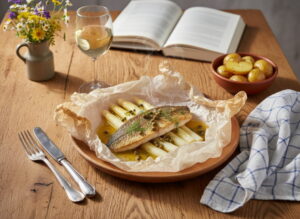 White asparagus with zander en papillote and caper butter, parcel opened on a white plate, Riesling white wine glass, Bavarian farmer's table