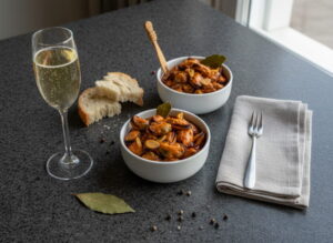 Mejillones en escabeche in white ceramic bowl, mussels shining in pimentón marinade, garlic and laurel visible, champagne glass with sparkling Albariño, Galician granite, Atlantic evening light, tablescape